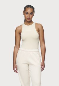 Body beige senza maniche realizzato in tessuto liscio, abbinato a comodi pantaloni felpa coordinati con tasche laterali e un logo sottile.