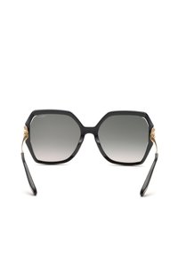 Lunettes de soleil hexagonales noires oversize avec verres gris dégradés et charnières décoratives dorées sur les branches.