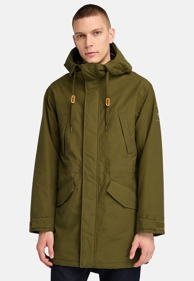 Olivgrön parkajacka med huva, utrustad med två framfickor, snörningsdetaljer och en texturerad tygfinish.