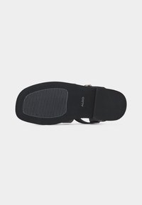 Semelle de sandale noire avec zone de grip texturée et branding ALDO, talon plat, vue par le dessous sur un fond clair uni.