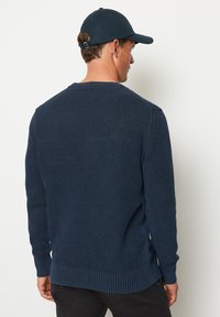 Dunkelblauer Strickpullover mit strukturiertem Muster, langen Ärmeln und gerippten Bündchen sowie Saum. Die Rückansicht zeigt ein klassisches Rundhalsdesign.
