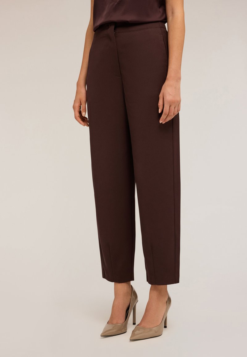 Pantaloni marroni su misura con gamba dritta, dotati di tasche frontali e una texture liscia, abbinati a scarpe con tacco alto beige.