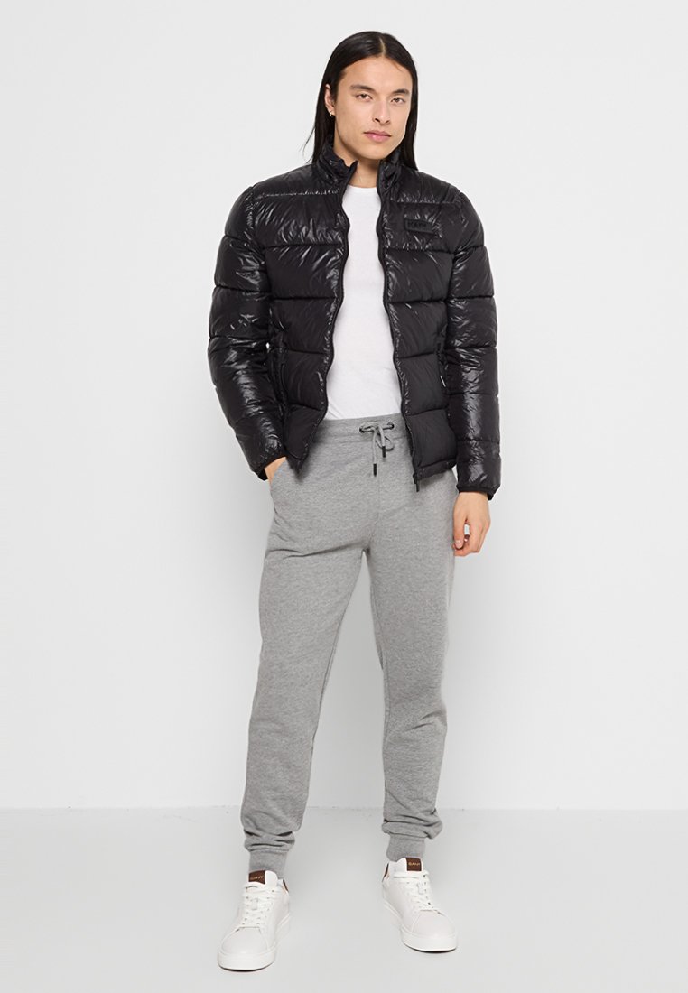 Chaqueta de plumas negra con cuello alto, acabado brillante y diseño acolchado. Combinada con pantalones de chándal grises y zapatillas blancas.
