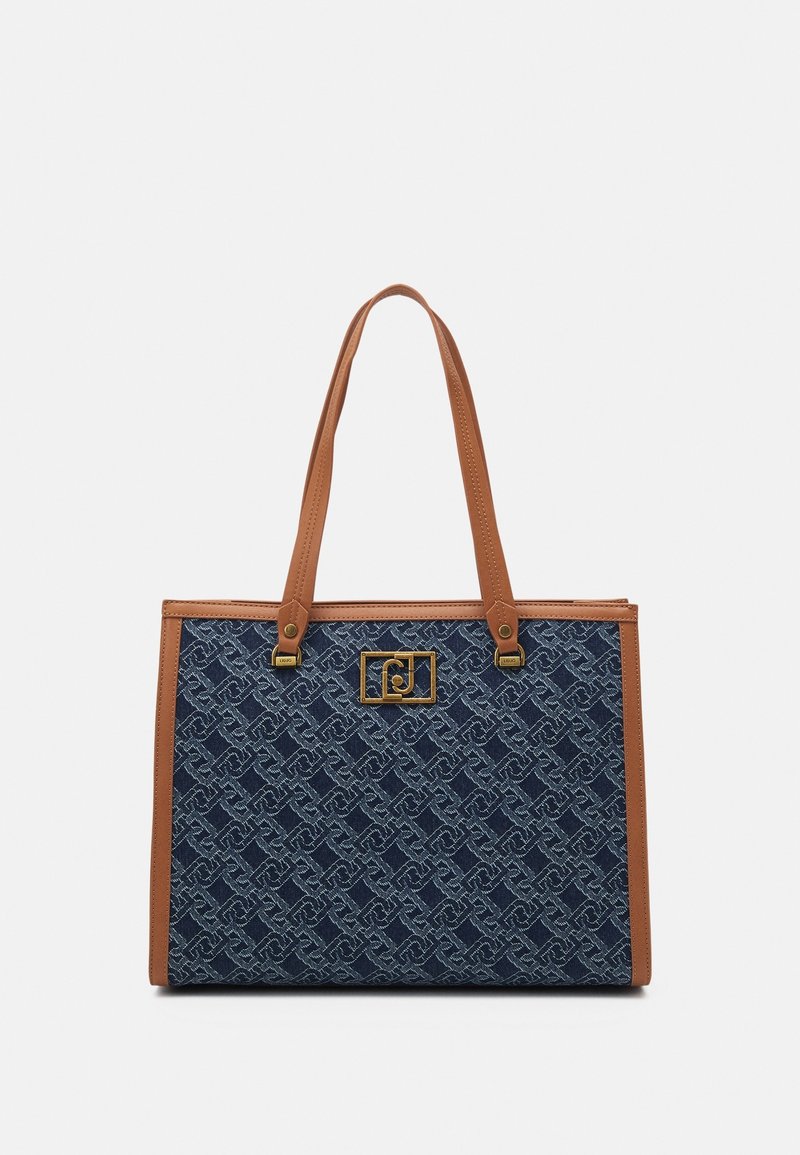 Sac cabas bleu à motif avec garniture en cuir marron et anses, avec une plaque logo rectangulaire dorée à l'avant.