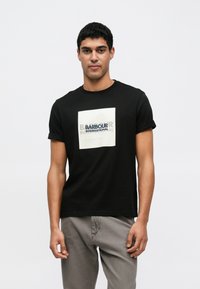 Fekete pamut póló, melyen egy négyzet alakú grafikán fehér és kék színű "BARBOUR INTERNATIONAL" felirat látható. Rövid ujjú, kerek nyakú.