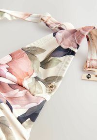 Lillelõngaga kangas, millel on roosa ja lilla lillemuster beežil taustal; sisaldab kuldset aksenti ja reguleeritava rihma detaili.