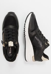 Černé tenisky s kombinací hladkých a strukturovaných panelů. Mají zlaté kovové prvky, boční zip a bílou podrážku pro kontrast.