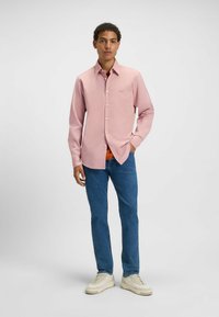 Lichtroze overhemddas met een gestructureerd patroon, gecombineerd met blauwe jeans en crèmekleurige sneakers. Bevat een subtiele merklogo op de borst.