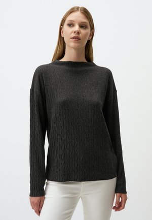 Pull en tricot gris charbon avec un motif en zigzag texturé, manches longues et encolure ras du cou. Porté par-dessus un pantalon blanc.