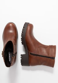 Botas de tobillo de cuero marrón con suela negra gruesa, cremallera lateral y detalles de costura, que muestran un diseño elegante de punta redondeada.