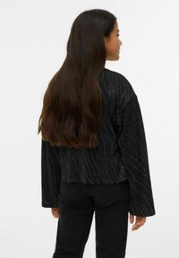 Juodas trumpintas megztinis ilgomis rankovėmis, su banguotu metaliniu raštu. Derinamas su juodais džinsais, kuriant kasdienį siluetą.