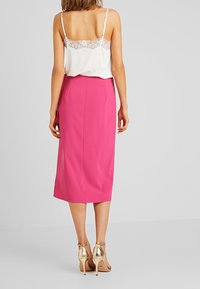 Roze midi-jurk met een nauwsluitende silhoutte en zijsplitten, gecombineerd met een witte kanten camisole en gouden strappy hakken. Gladde stoftextuur.