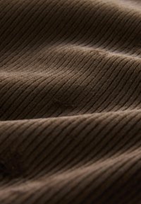 Braunes Cordstoffgewebe mit vertikalen Rillen, weicher Textur und leicht glänzender Oberfläche. Das Material wirkt dick und einladend.