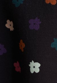 Tessuto nero con piccoli motivi floreali colorati in teal, viola, arancione e beige, caratterizzato da una superficie texture.