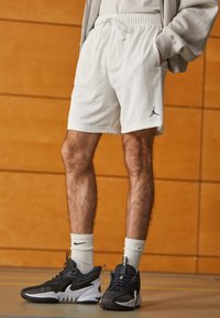 Fehér sportos rövidnadrág perforált textúrával és rugalmas derékkal, fekete sportcipővel és fehér, bokáig érő zoknikkal párosítva. A nadrágon Jordán logó látható.