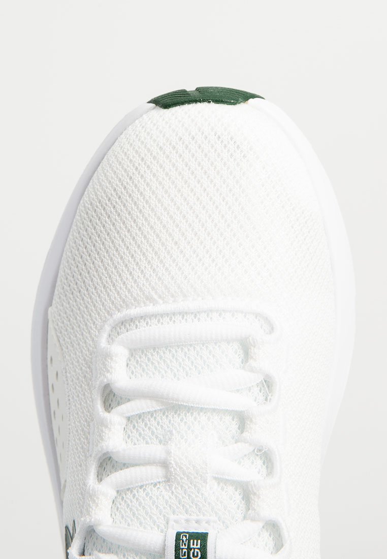 Zapatilla de malla blanca con una superficie texturizada, que presenta un sistema de cierre con cordones blancos, un detalle verde en el talón y un diseño ligero.