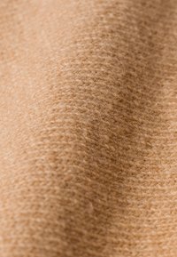 Gros plan sur un tissu en laine beige doux et texturé montrant un motif de tricot fin et des fibres superficielles duveteuses.