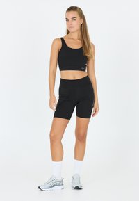 Zwarte sportieve crop top en korte broek met een aansluitend ontwerp. De outfit beschikt over een soepele stof en subtiele stikdetails. Sportieve schoenen en witte sokken.