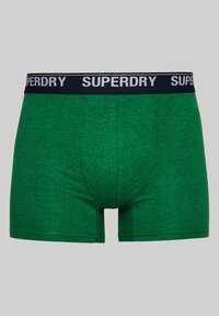 Groene katoenen boxershorts met een marineblauwe elastische tailleband waarop "SUPERDRY" in witte letters staat. Smooth textuur en een aansluitend ontwerp.