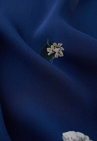 Marineblaues Gewebe mit strukturierter Oberfläche, das kleine florale Muster in Weiß und Grün aufweist und einen subtilen visuellen Kontrast erzeugt.