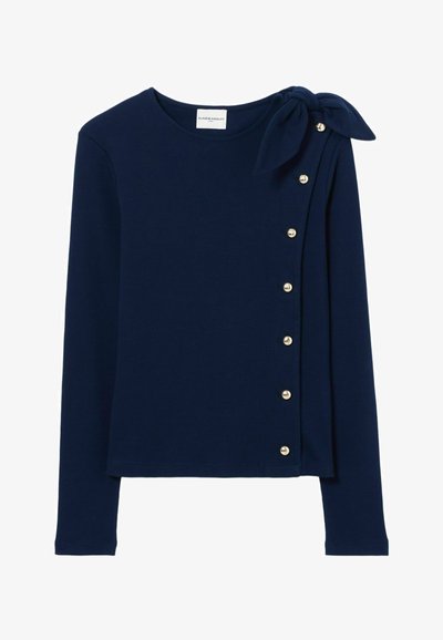 Top lungo navy con dettaglio a fiocco sulla spalla sinistra, bottoni decorativi ai lati e una texture di tessuto liscia.