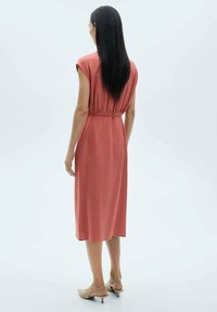 Abito midi, realizzato in tessuto morbido di un colore corallo tenue, con maniche a cappuccio corte e una cintura elastica. Design semplice.