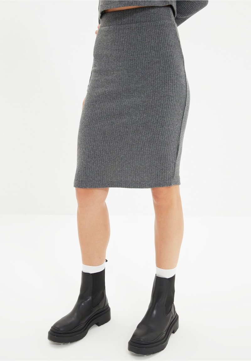 Jupe midi gris côtelée avec une silhouette ajustée et une taille haute. Associée à des bottines noires avec une semelle épaisse et des panneaux latéraux élastiques.