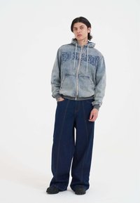 Hooded, zip-up, light blue denim jacket with "ED HARDY" print; paired with wide-leg dark blue jeans and black shoes.