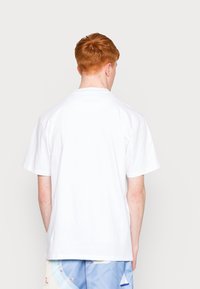 Camiseta de algodón blanca con mangas cortas y cuello redondo, mostrada desde la parte de atrás. Textura suave, sin patrones o acentos visibles.
