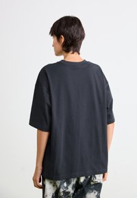 T-shirt en coton noir surdimensionné avec un col rond, des manches courtes et une texture lisse. Le dos présente un design simple et sans fioritures.
