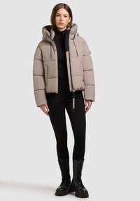 Beżowa kurtka puchowa z kapturem, z poziomymi przeszyciami, kieszeniami z przodu i zapięciem na zamek. Połączona z czarnymi legginsami i butami wojskowymi.