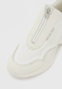 Weißer Sportschuh aus Mesh- und glatten synthetischen Materialien, mit einem Frontreißverschluss, dezenten silbernen Akzenten und einer gepolsterten Sohle.