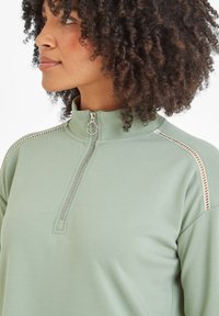 Light green zip-up sweatshirt with a stand collar, featuring silver zipper and decorative stitching along the shoulders. Smooth fabric texture.