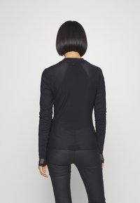 Haut noir à manches longues au design ajusté, avec des panneaux en maille aux épaules et un tissu texturé. Des détails incluent des encoches pour les pouces aux manches.