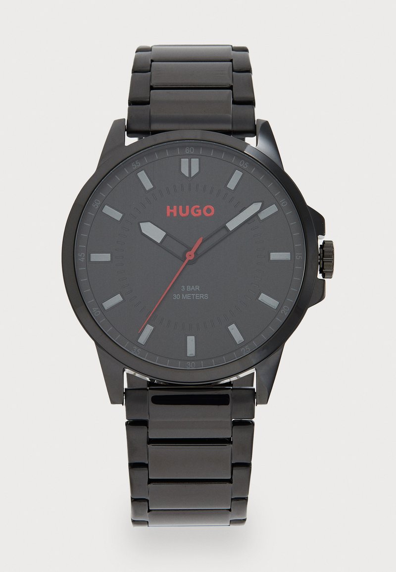 Zwart roestvrijstalen horloge met een ronde wijzerplaat, matte zwarte wijzerplaat, rode accenten, zilveren uurmarkeringen en een drievoudige schakelband. Waterbestendig tot 30 meter.