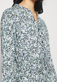 Blumenmuster-Kleid in Shirt-Form mit Knopfleiste, Kragen und langen Ärmeln. Der Stoff ist leicht und in Blau-, Grün- und Weißtönen gehalten.