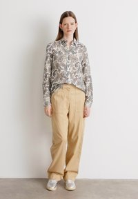 Camisa de botão de manga longa com padrão paisley em cores suaves; combinada com calças largas bege e ténis cinzentos.