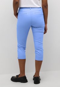 Pantaloni blu cropped realizzati in tessuto liscio, con tasche posteriori e un design affusolato. Indossati con scarpe nere senza lacci.