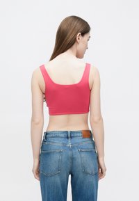 Top rosa justo e curto com alças largas, com tecido suave e um design traseiro limpo. Combinado com jeans azuis de cintura alta.