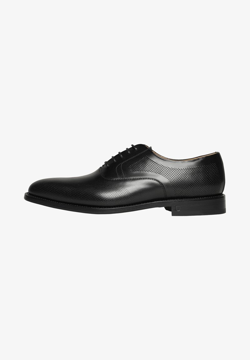 Chaussure habillée en cuir noir avec un design perforé, bout arrondi, fermeture à lacets et semelle en caoutchouc à profil bas, présentant de subtils accents tonals.
