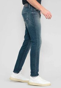 Skinny jeans in vervaagd blauw denim, met een gladde textuur, vijf zakken en subtiele stikdetails, gecombineerd met witte sneakers.
