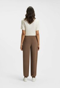 Bruine broek met een taps toelopende pijp, met zijnaad en een zachte textuur. Gecombineerd met een kortärm, off-white top gemaakt van lichte stof.