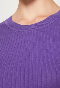 Primo piano del collo e della parte superiore del torace di una persona che indossa un maglione a girocollo rigato di colore viola.