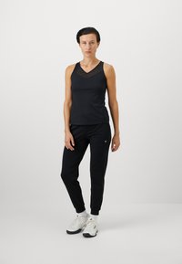Svart treningstopp i tank-modell med netting v-halsdesign, kombinert med svarte joggebukser og hvite treningssko. Enkel, funksjonell treningstøy.