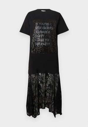 Czarna sukienka-tunika z panelem cekinowym z białym napisem, warstwowa z przezroczystą czarną koronkową spódnicą. Okrągły dekolt i krótkie rękawy.