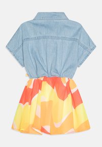 Denim top s krátkým rukávem se skládáním v pase, kombinovaný s živou sukní s oranžovo-žlutým vzorem, hladká textura a hravý design.