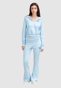Haut coupe cropped bleu clair avec un col en V, une poche avant et des accents en argent, associé à un pantalon évasé assorti avec une broderie de logo.