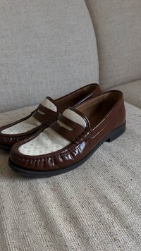 Mocassini in pelle marrone con tessuto beige decorato sulla parte superiore, caratterizzati da un accento cucito e una suola piatta in gomma nera.