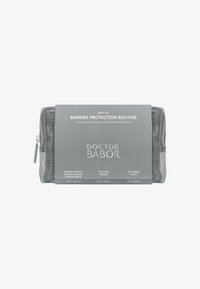 Pochette zippée grise avec texture en maille, étiquetée "Doctor Babor", incluant du texte concernant des produits de soins de la peau pour protection barrière en police noire élégante.