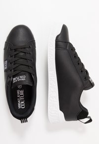 Černé syntetické tenisky s kulatou špičkou, šněrovacím designem, texturovaným černým svrškem a bílou gumovou podrážkou s vyraženými detaily loga.